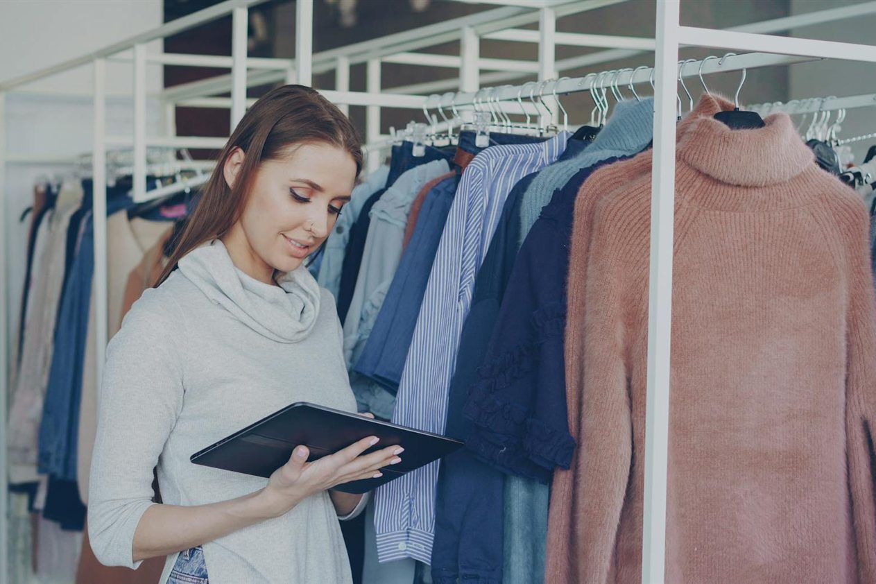 Fashion stylist using a tablet next to a clothing rack for a fashion apps comparison guide