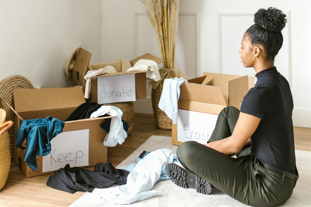 Person sorting clothes into keep, donate, and trash boxes during a closet cleanout